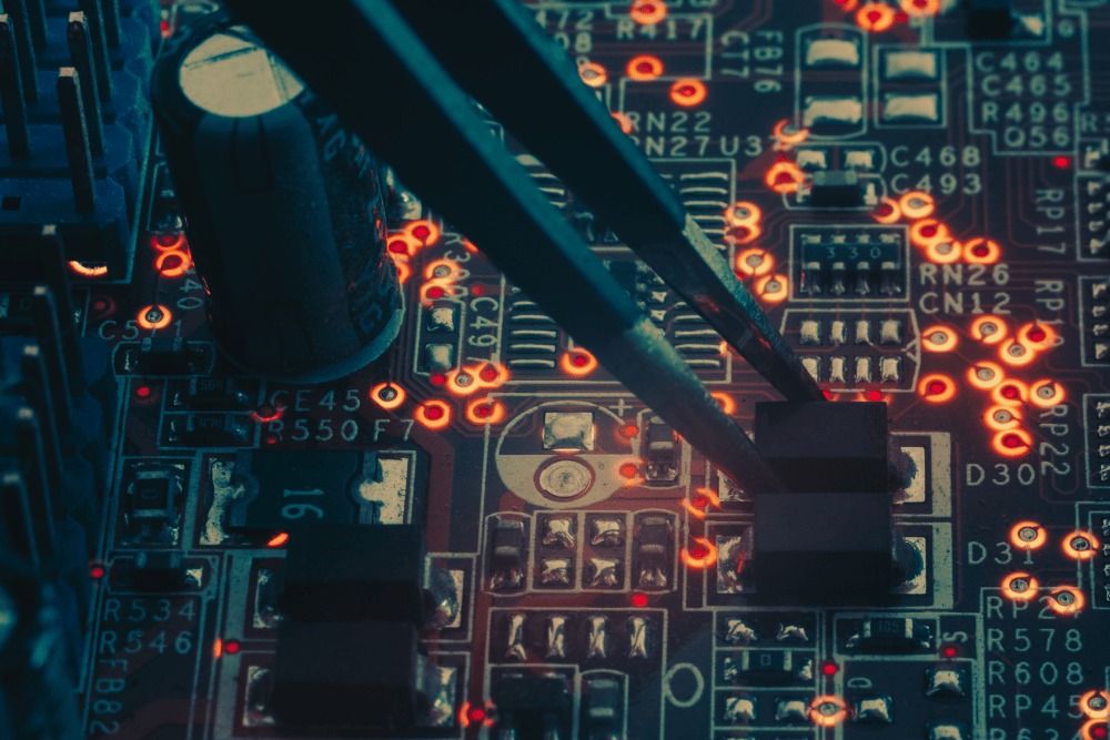 Close-up of a circuit board with tweezers holding an electronic component, highlighting glowing red solder points.