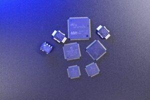 An assortment of integrated circuit (IC) chips from different manufacturers arranged on a dark surface with blue lighting.